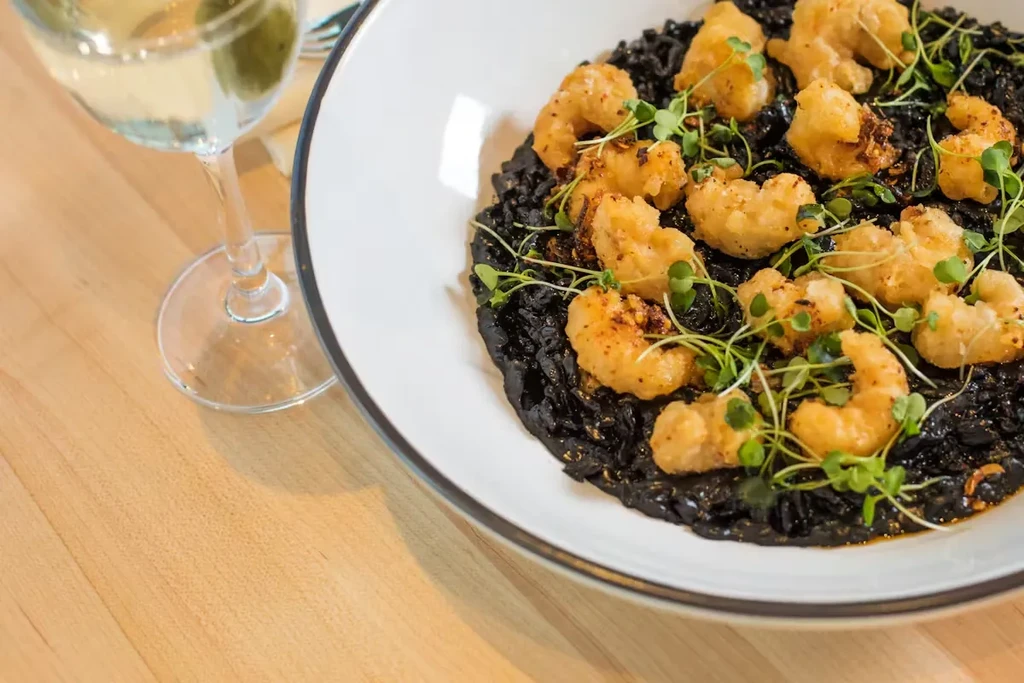 Squid ink risotto with fried shrimp, microgreens, and wine.