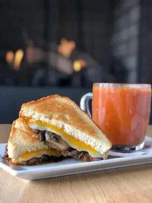 Half-cut toasted sandwich showing melted cheese, mushrooms, and a drink.