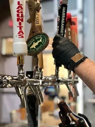 Hand in glove pours beer from Lagunitas, Dogfish Head, Narragansett taps.