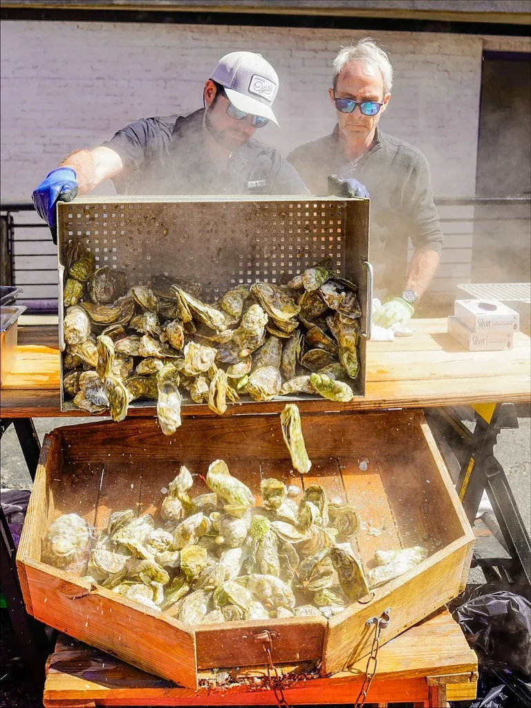 Two men pour steaming oysters from a crate into a bin.