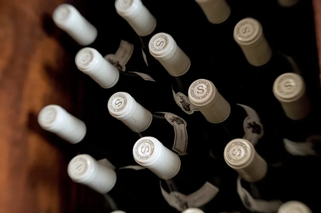 Close-up of wine bottles with 'Schug Winemaster' caps, stored horizontally.