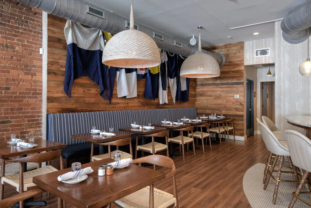Restaurant dining area with brick, wood, striped booth, nautical flags.