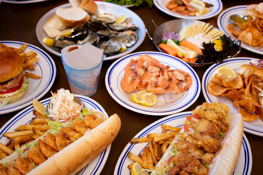 Table laden with various seafood dishes, including po'boys, oysters, and shrimp.