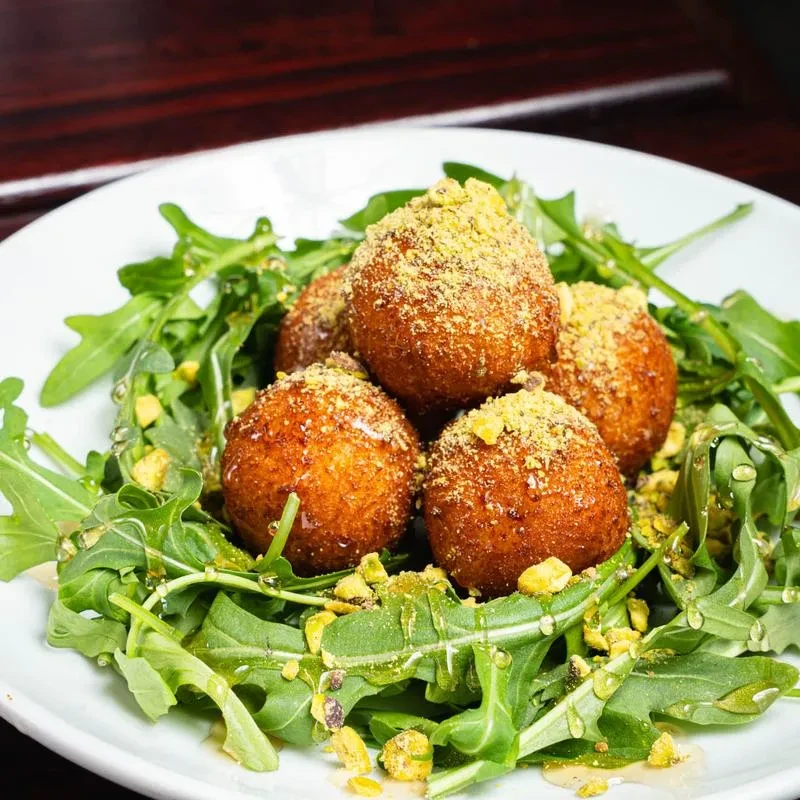 Five golden fried balls dusted with pistachios on arugula.