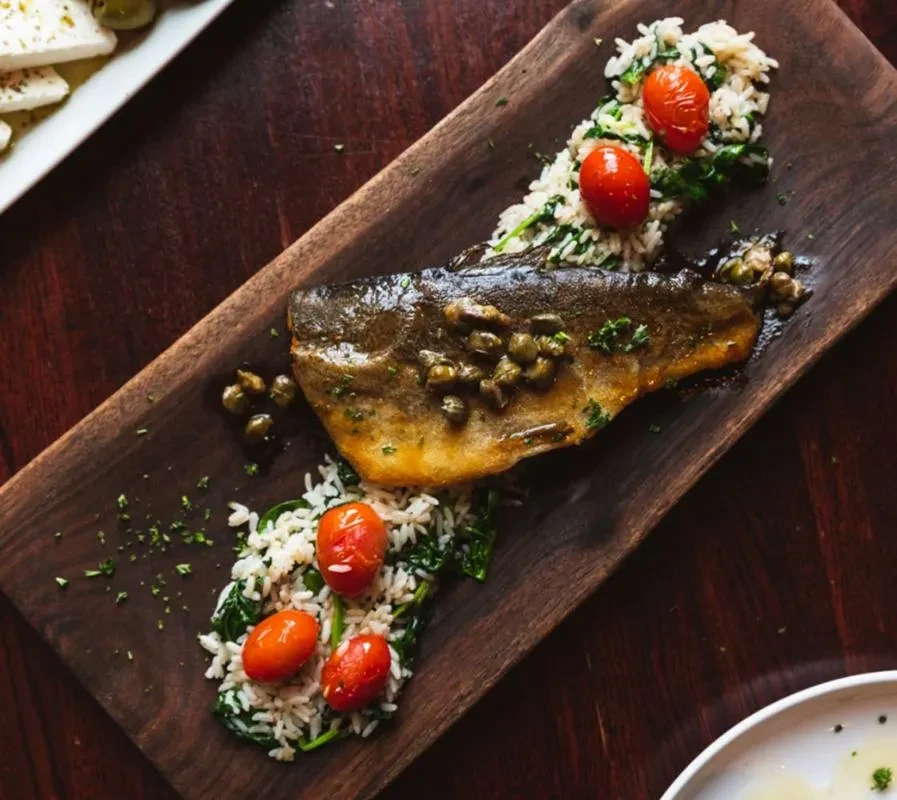Pan-seared fish with capers, served with rice, greens, and tomatoes.