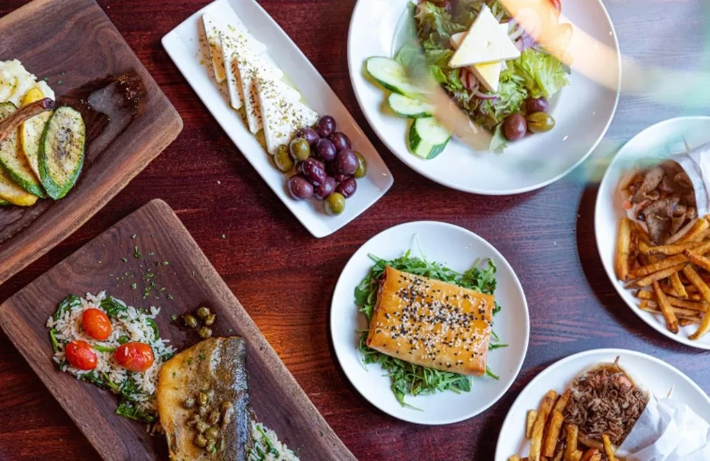 Diverse Mediterranean dishes and wraps served on a wooden dining table.