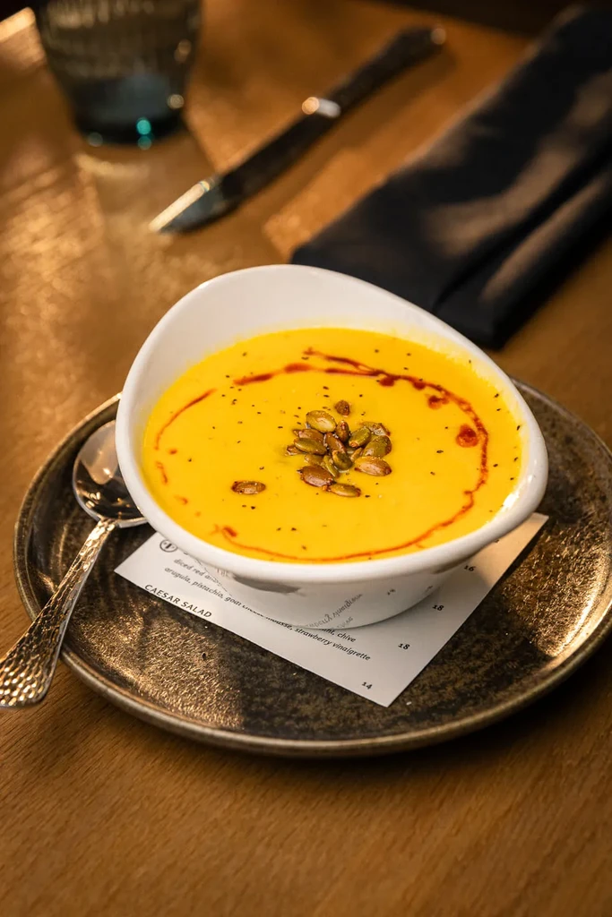 Creamy yellow-orange squash soup with pumpkin seeds and oil swirls.