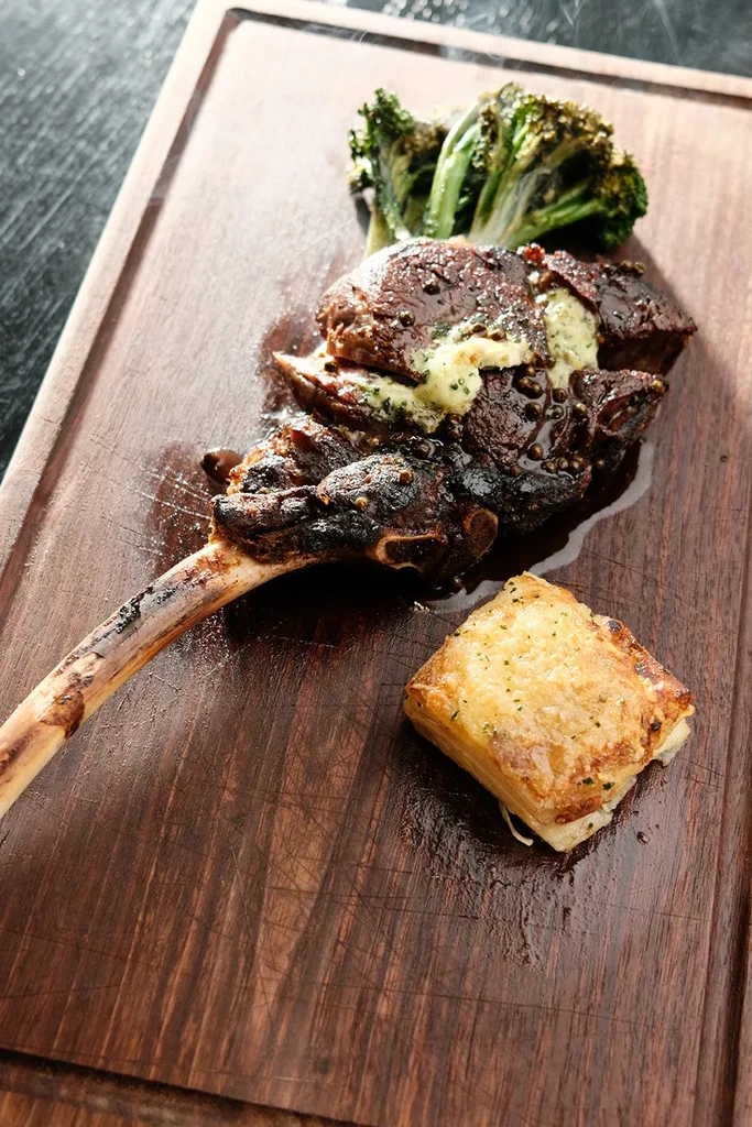Gourmet roasted meat, broccoli, and tart on a dark wood board.