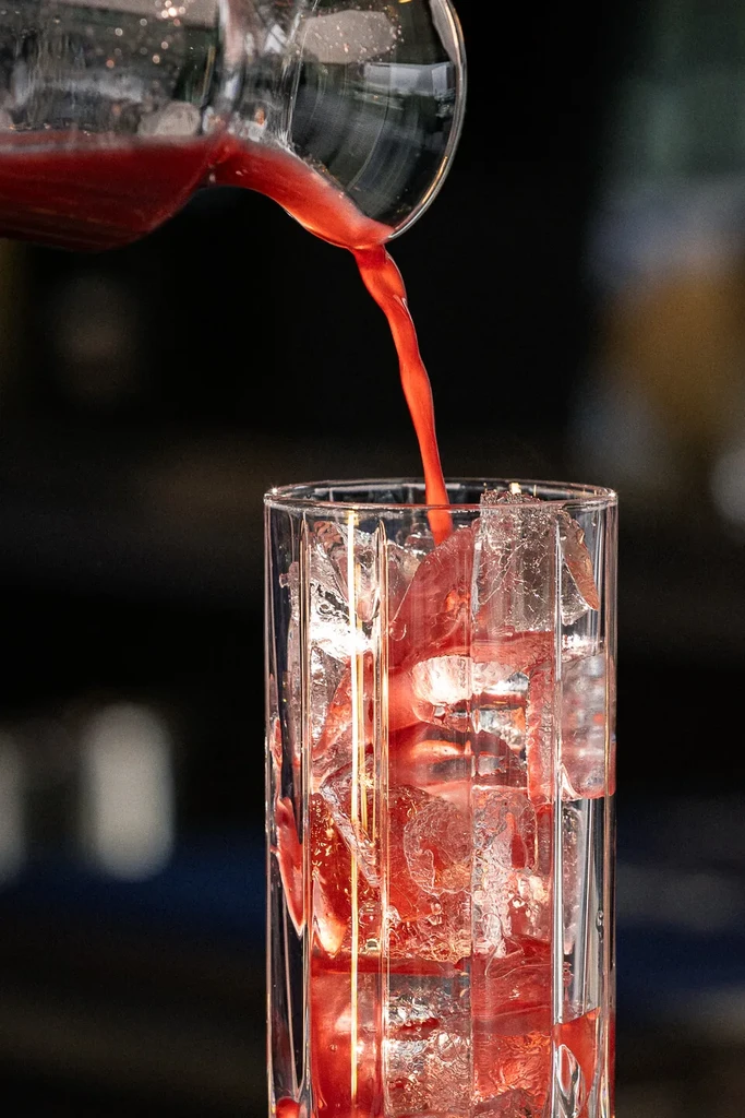 Red beverage poured from a pitcher into an iced glass.