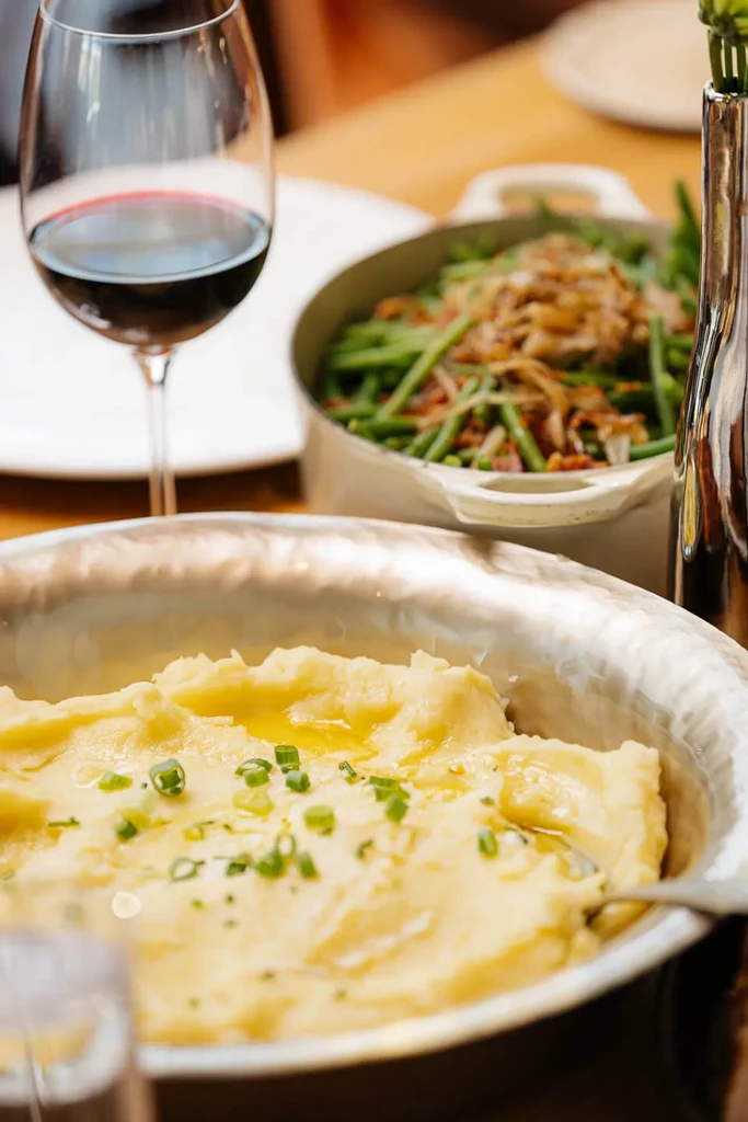 Creamy mashed potatoes, red wine, green beans on a wooden dining table.