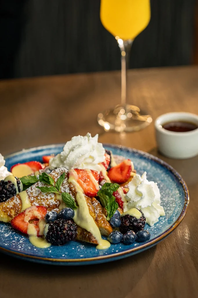 French toast topped with berries, whipped cream, mint, and powdered sugar.
