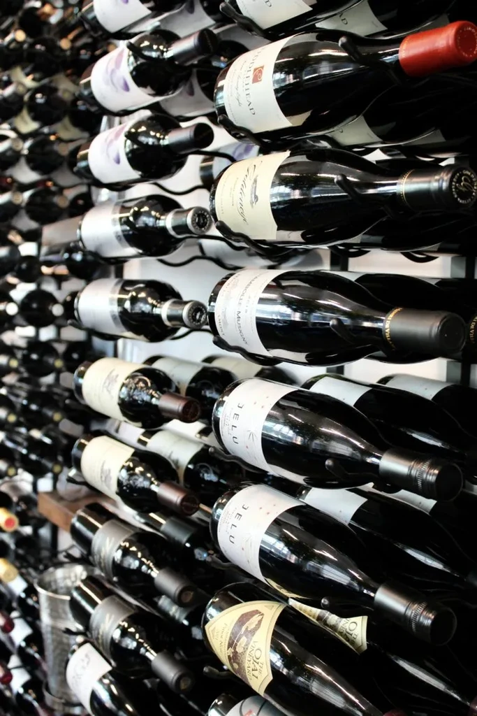 Many red wine bottles neatly displayed in a dark wall-mounted rack.