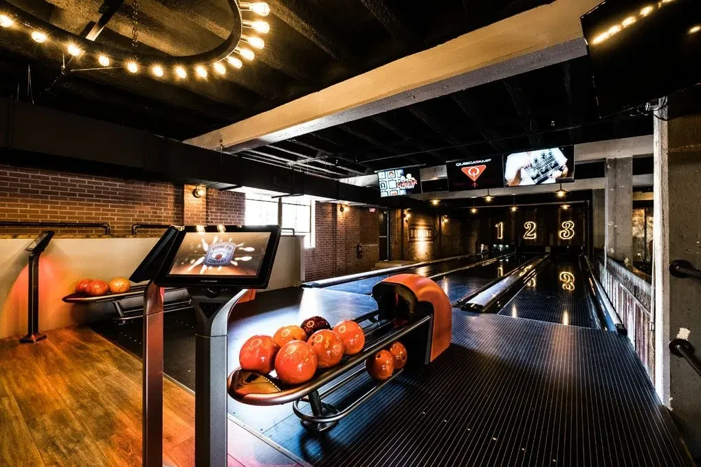 Modern, upscale bowling alley with multiple lanes, industrial-chic decor, warm lighting.