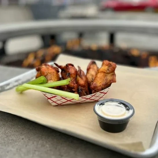 Fried chicken wings, celery sticks, and white dip in a checkered boat.