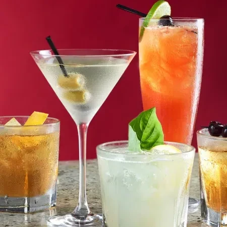 Five garnished cocktails on a speckled countertop with a red background.
