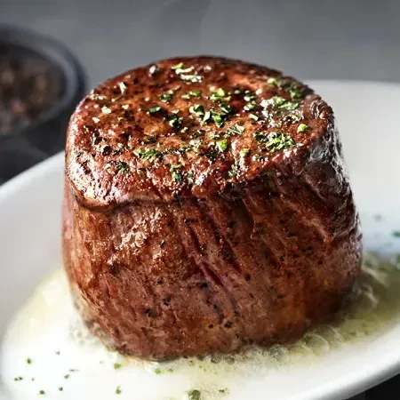 Seared steak with herbs and butter on a white plate.