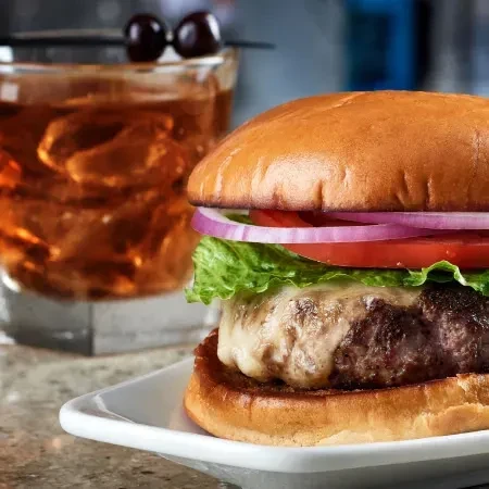 Golden cheeseburger, amber cocktail with cherries, speckled counter.