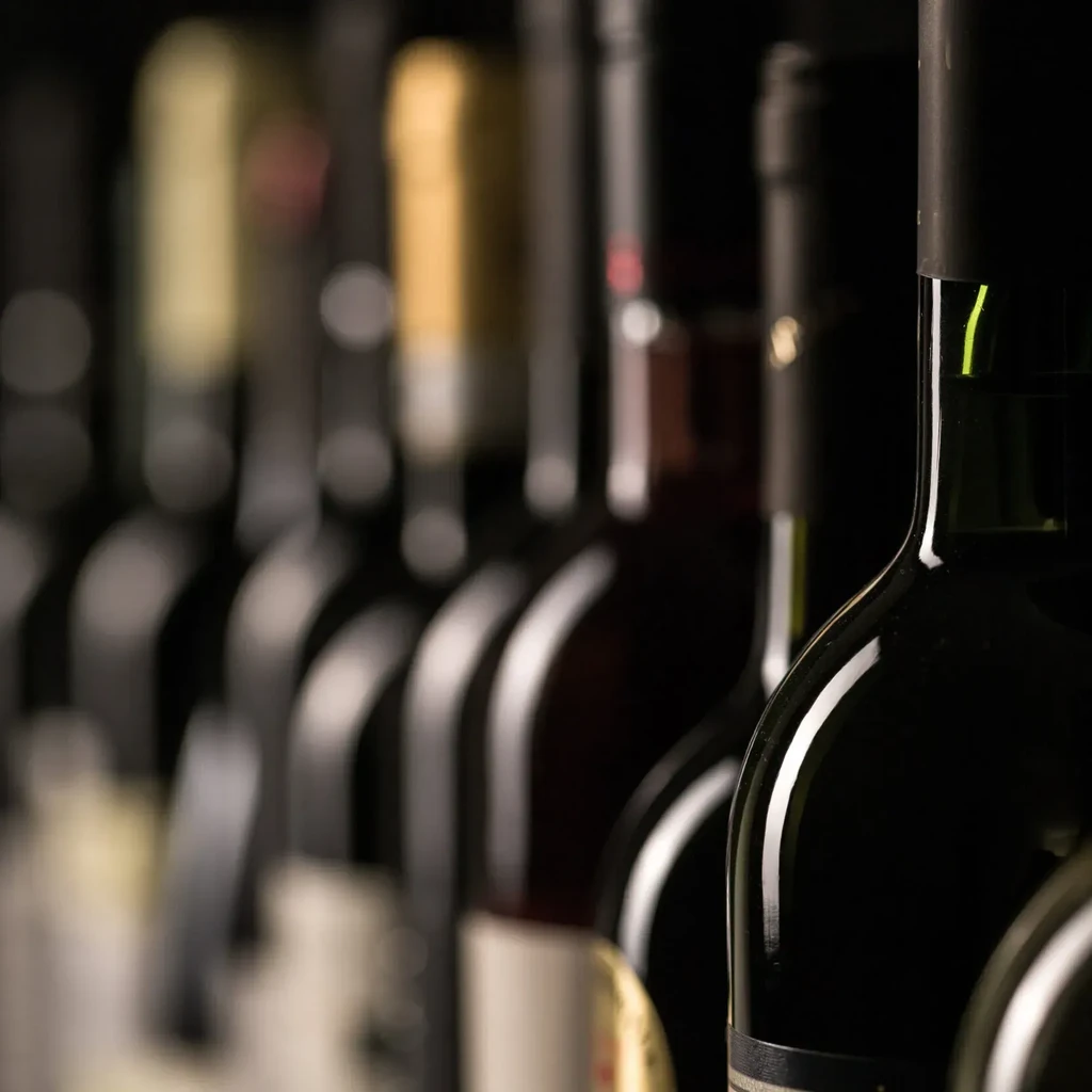 Dimly lit row of wine bottles, one green bottle in focus.