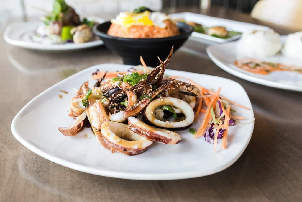 Close-up of grilled squid on a white plate with green onions and sesame.