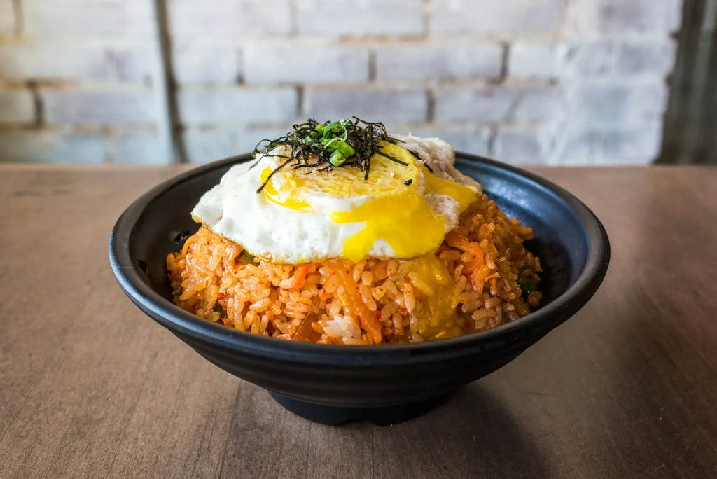 Orange fried rice in bowl with sunny-side-up egg, nori, chives.