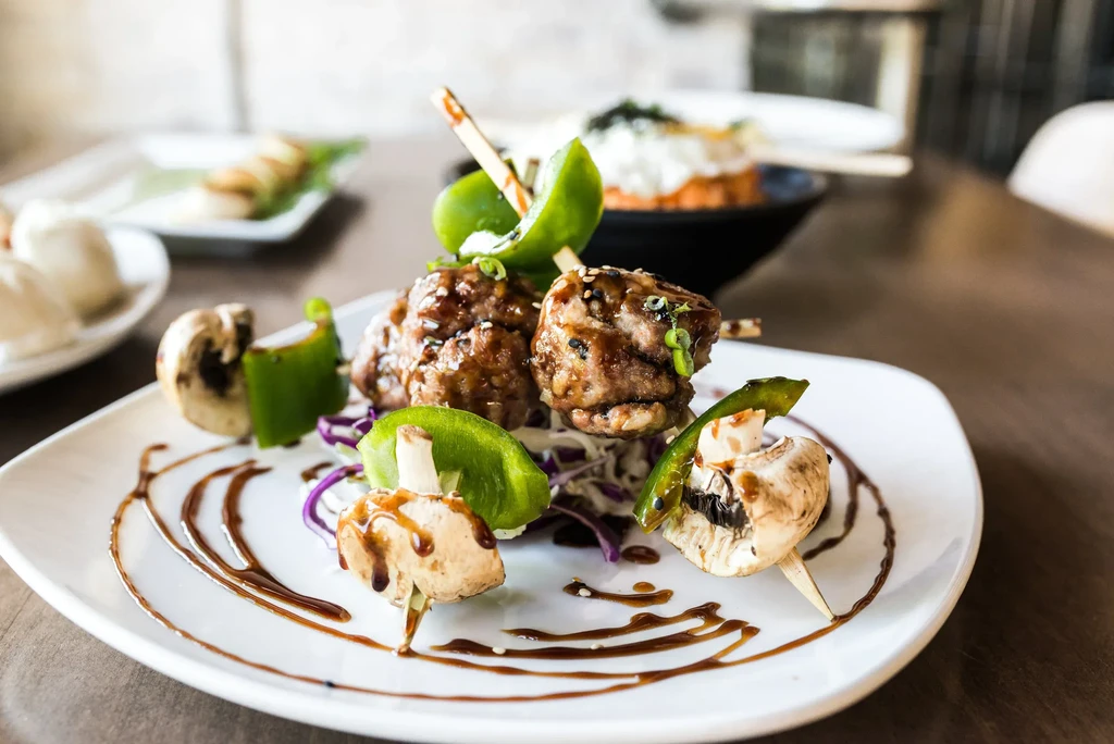 Plated glazed meatballs skewers with cabbage, mushrooms, bell peppers, and sauce.