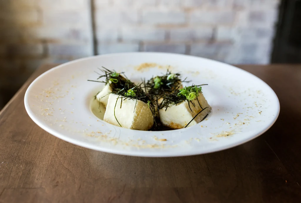 Close-up of golden-brown fried tofu topped with seaweed and scallions.