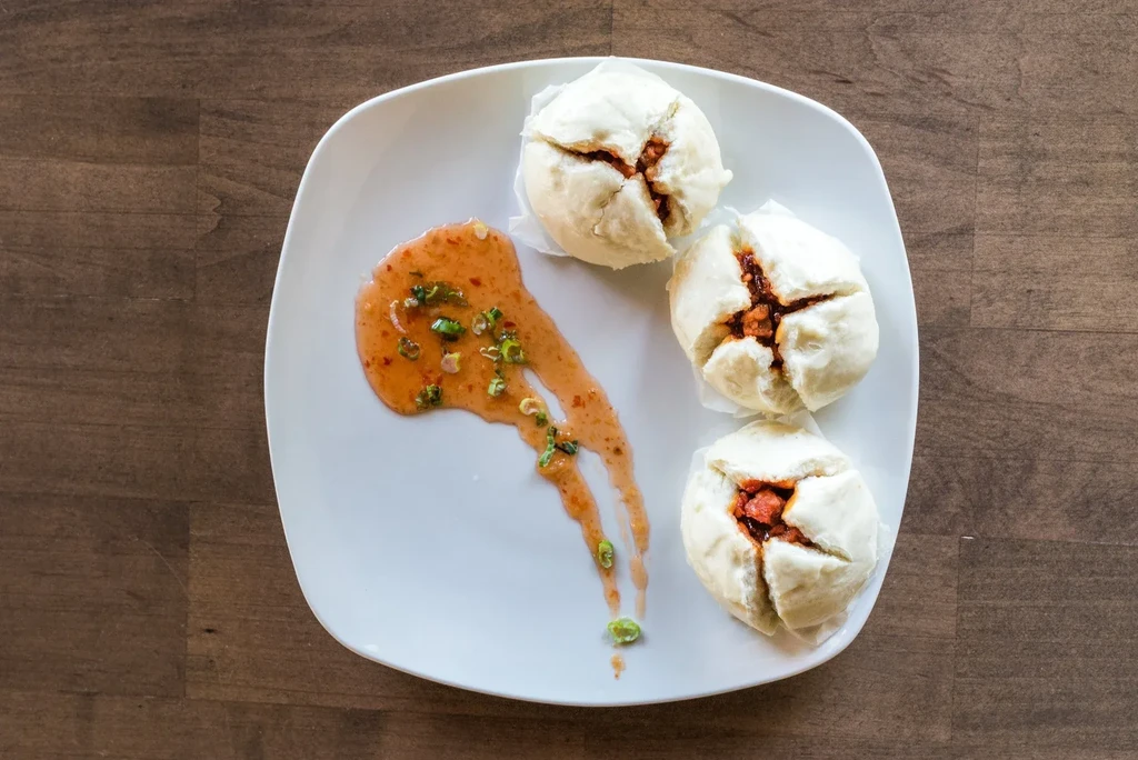 Three steamed buns with red filling and orange sauce on a plate.
