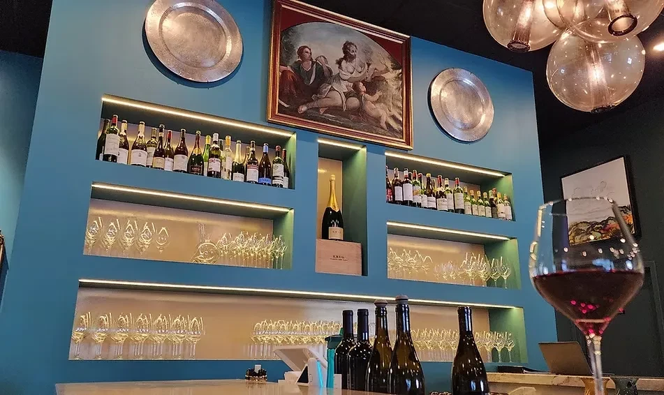Sophisticated wine bar with teal wall, illuminated shelves, and classical painting.