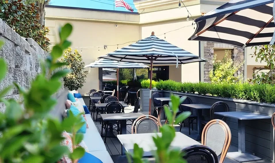 Empty outdoor dining patio with tables, striped umbrellas, and plants.
