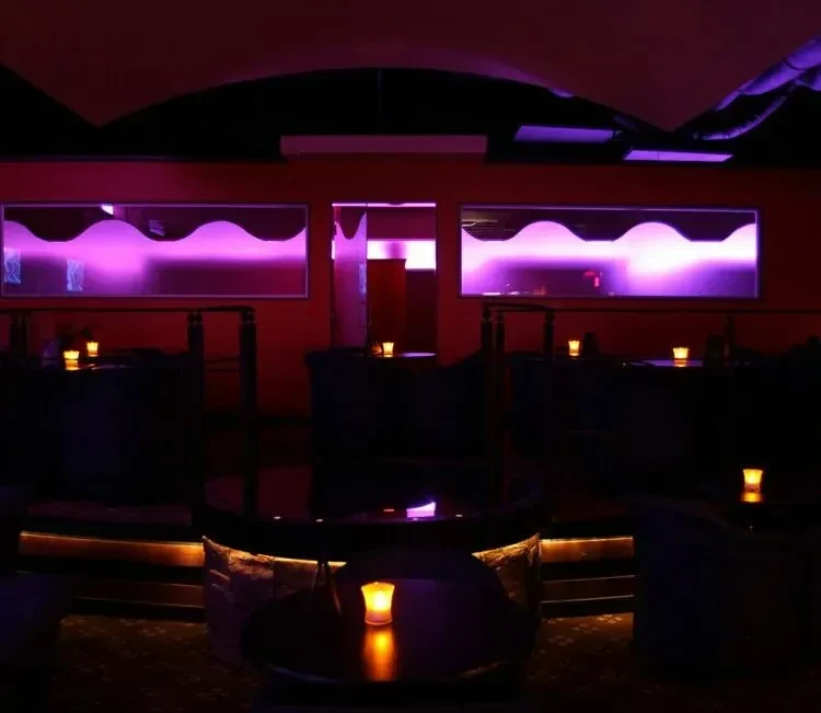 Dimly lit bar interior, purple reflections, and warm table lights.