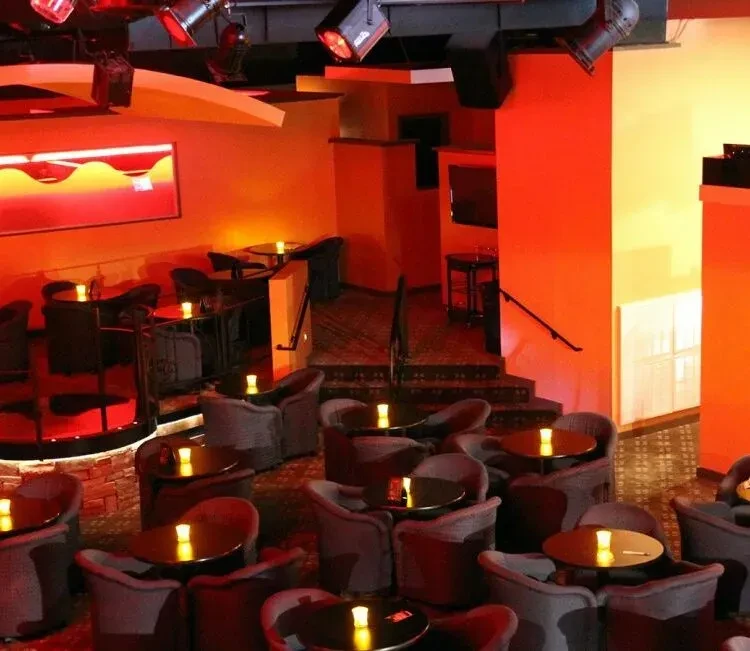 Empty, multi-level bar interior with dramatic red lighting and candlelit tables.