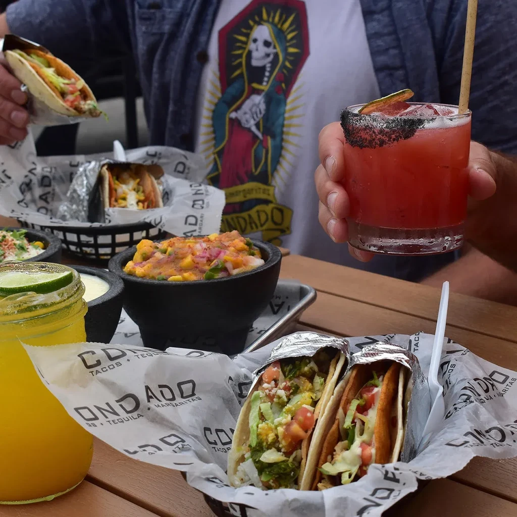 Person holding tacos and cocktails at a Condado Tacos restaurant.