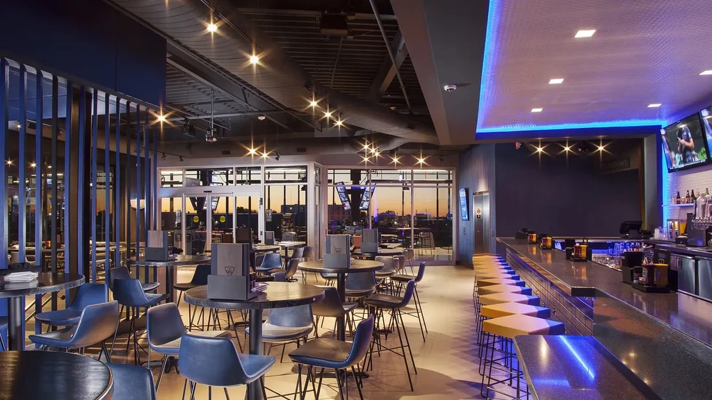 Modern bar interior with blue seating, long bar, and sunset city view.