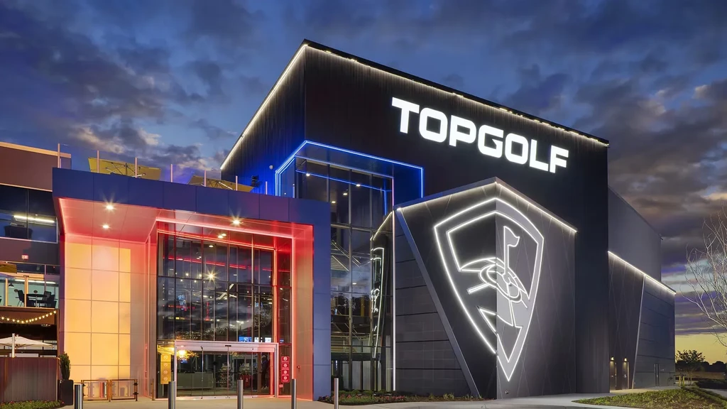Modern TOPGOLF building exterior illuminated by colorful LEDs at night.