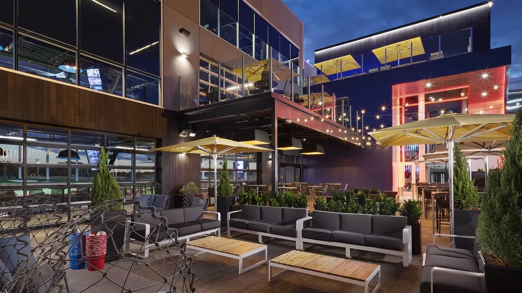 Multi-level complex at dusk, featuring golf bays and outdoor dining patios.