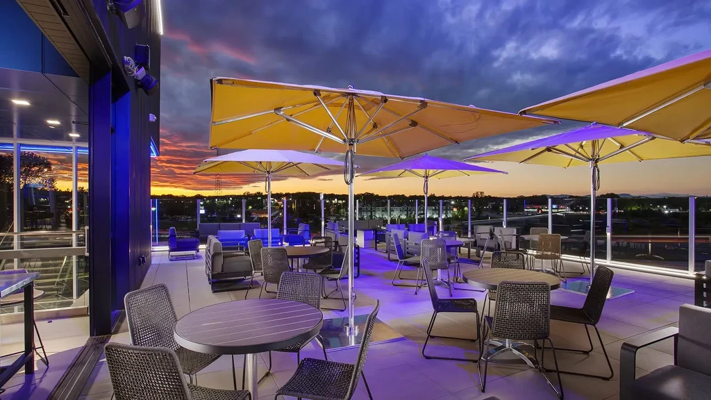 Empty modern rooftop patio with yellow umbrellas, purple light, and sunset cityscape.