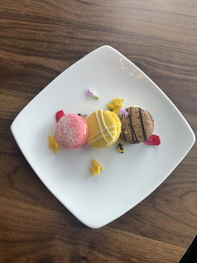 Pink, yellow, and brown macarons on a white plate with flowers.