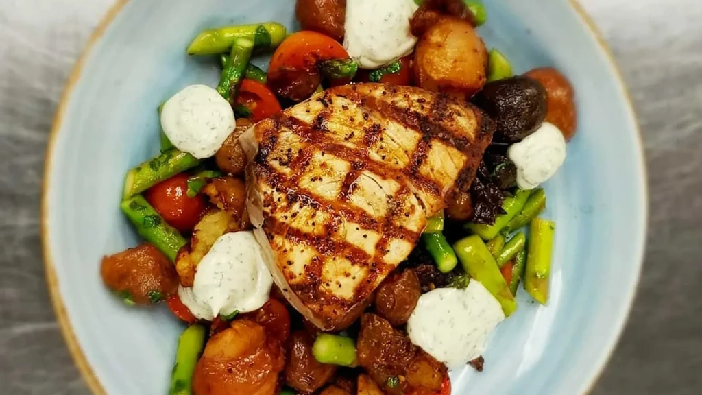 Grilled fish steak, asparagus, tomatoes, and creamy sauce in a blue bowl.