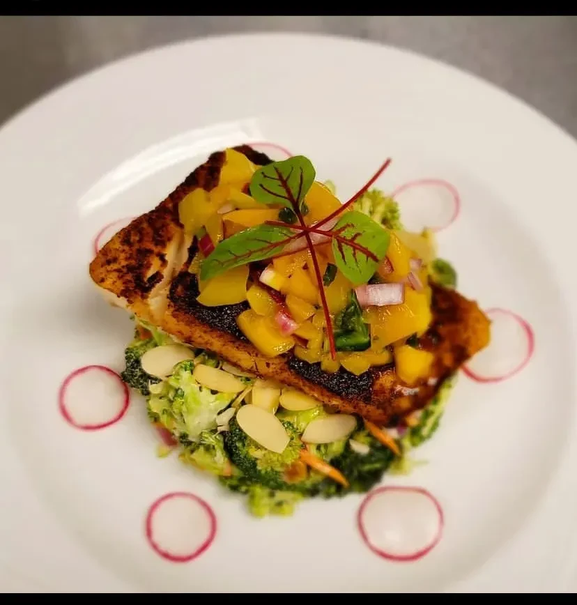 Plated pan-seared fish, vibrant mango salsa, broccoli salad, radishes.