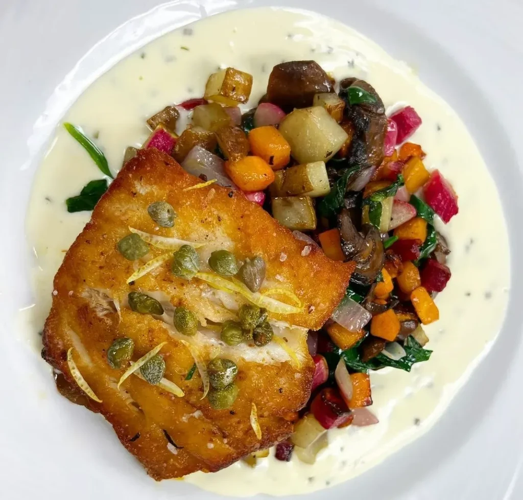 Pan-seared fish with capers and lemon zest, alongside roasted vegetables.