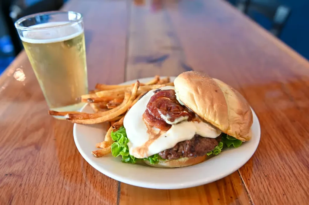 Gourmet burger, golden fries, and a foamy amber drink on wood.