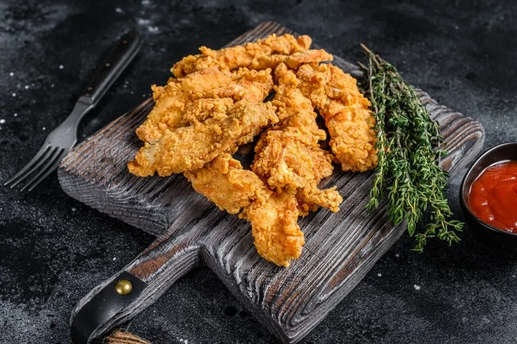 Crispy fried chicken tenders, dipping sauce, and herbs on wood.