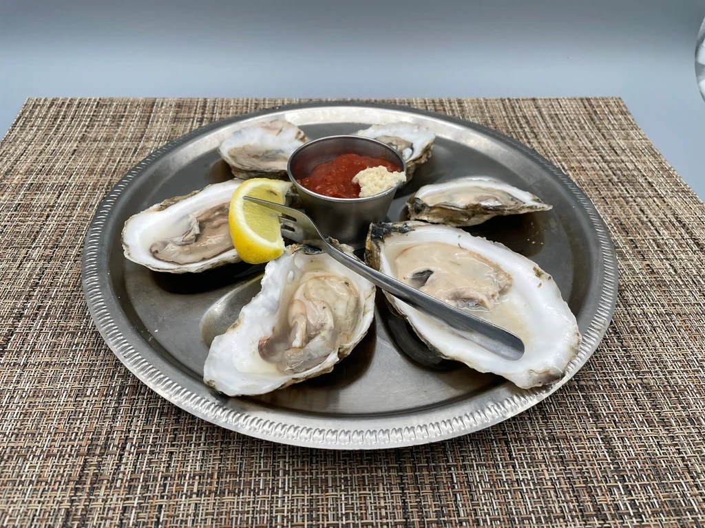 Six raw oysters on the half shell with sauce, lemon, and forks.