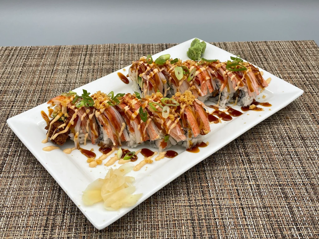 Sushi rolls topped with imitation crab, sauces, green onions, ginger, and wasabi.