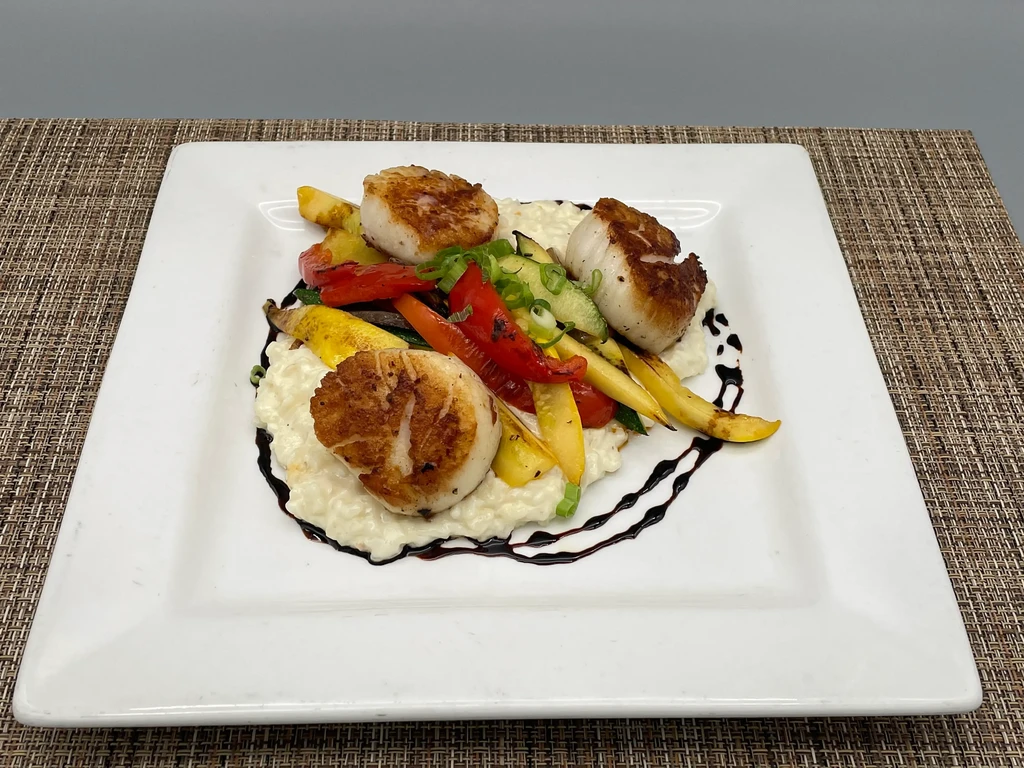 Pan-seared scallops with risotto, vegetables, and a dark balsamic glaze.
