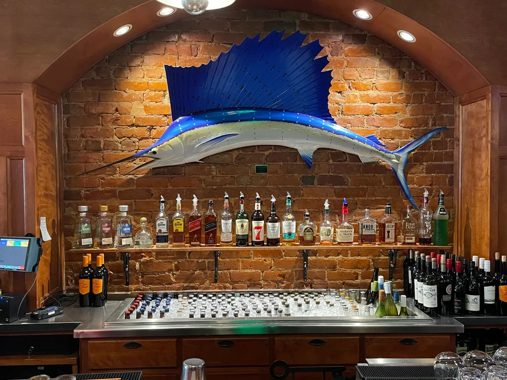 Restaurant bar with a prominent blue marlin sculpture on a brick wall.