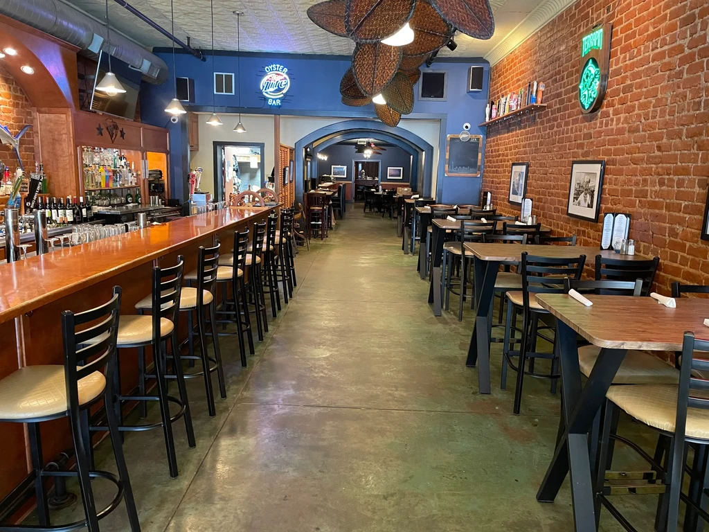 Spacious empty restaurant interior features a bar, brick walls, and neon signs.