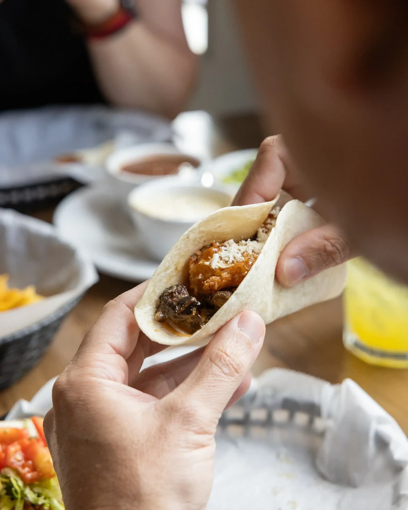 Close-up of hands holding a taco with fish, cheese, and sauce.