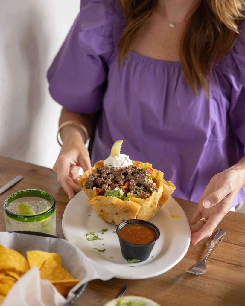 Top-down: Taco salad in a fried tortilla bowl, chips, salsa, margarita.