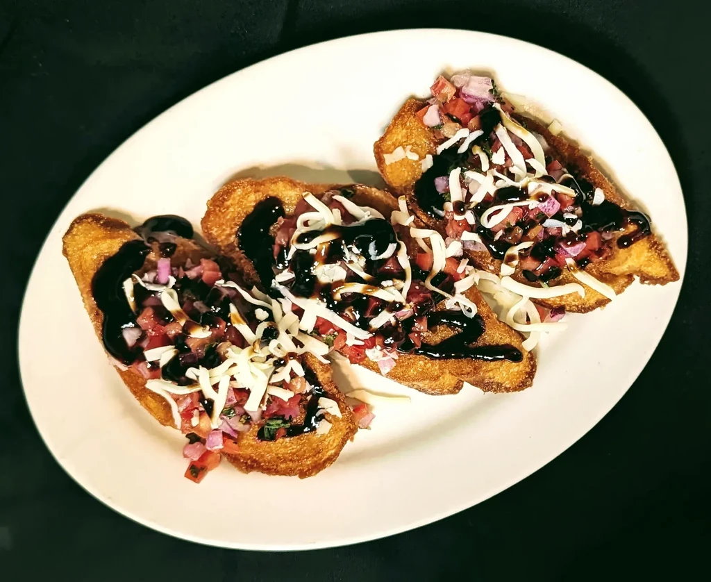 Three golden bruschetta with tomatoes, white cheese, and balsamic glaze.
